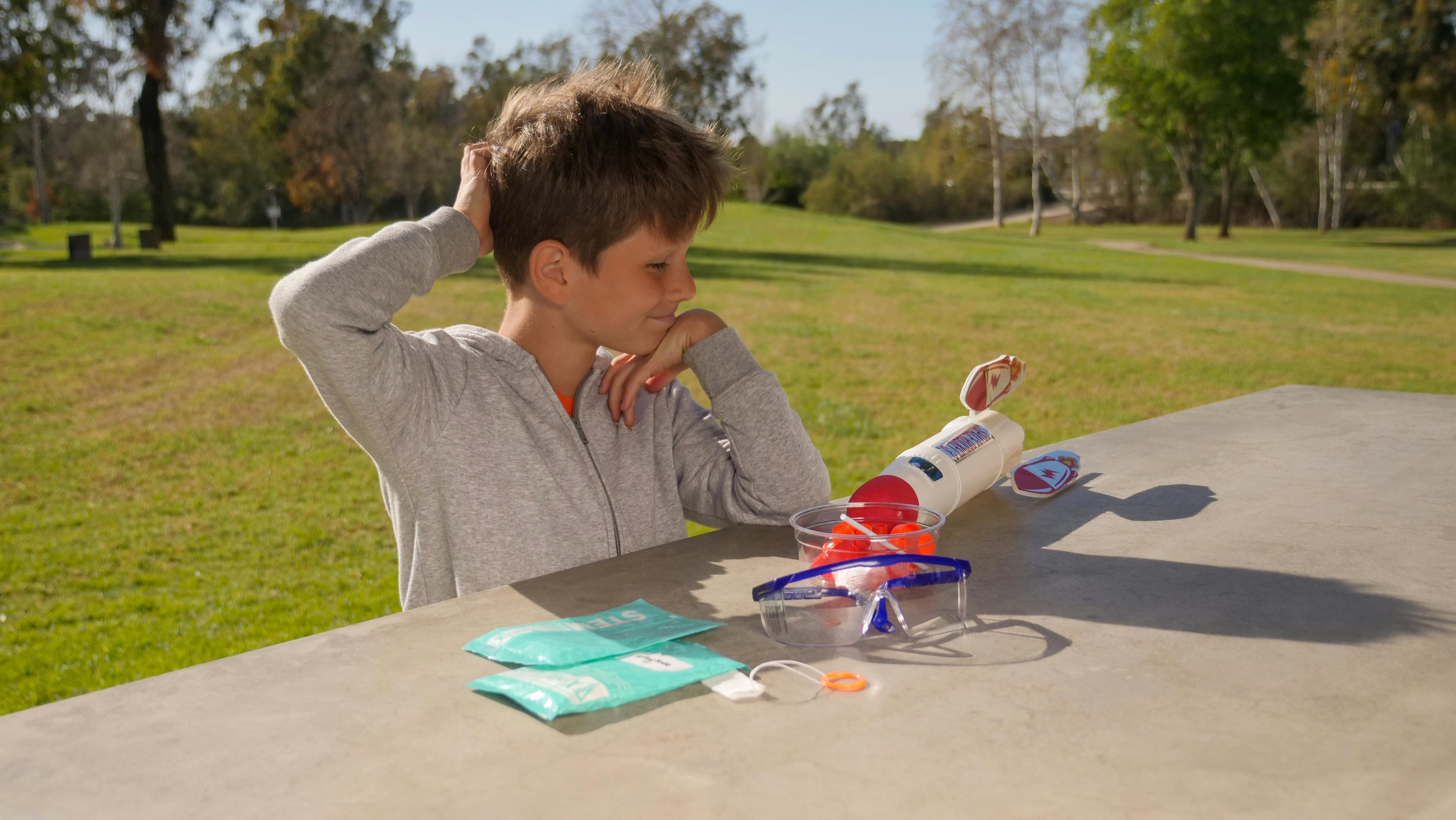 Kid sitting beside a toy rocket ship outdoors